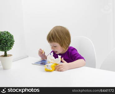 cute little girl eating a cookie while playing games on tablet computer at home