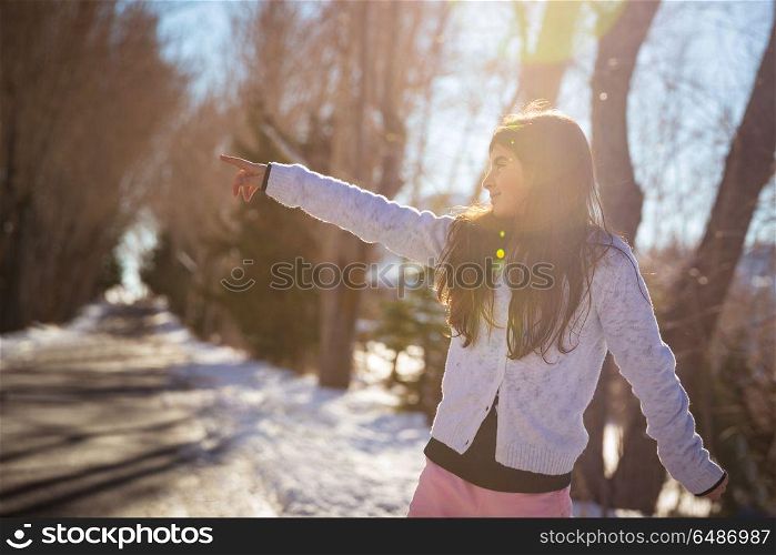 Cute little girl having fun outdoors in the winter park on sunny day, points to something with her hand, happy active winter holidays. Happy little girl in the winter park