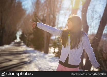 Cute little girl having fun outdoors in the winter park on sunny day, points to something with her hand, happy active winter holidays. Happy little girl in the winter park