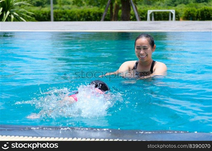 Cute little girl having fun swimming with her mother in the pool on a sunny day. Happy family, mother and her daughter playing in the swimming pool. Summer lifestyle concept.