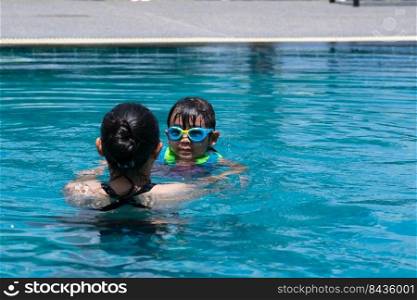 Cute little girl having fun swimming with her mother in the pool on a sunny day. Happy family, mother and her daughter playing in the swimming pool. Summer lifestyle concept.