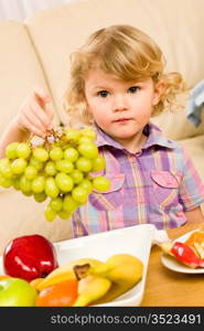 Cute little girl hold grapes healthy fruit bowl at home