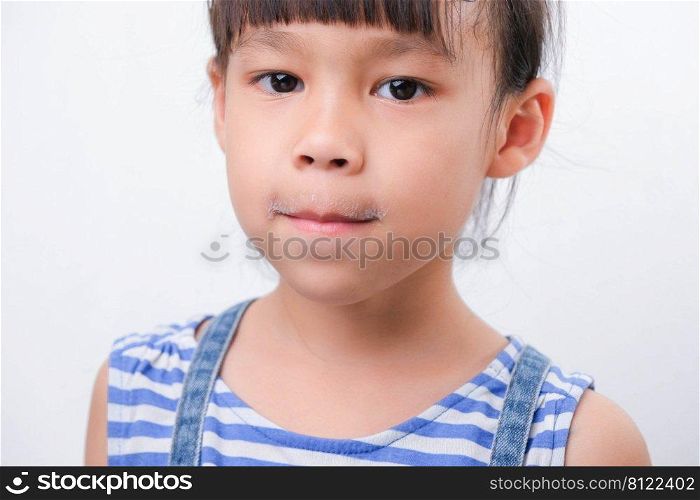 Cute little girl holding a glass of milk and licking her lips on white background. Small girl at home with smiling face, feeling happy enjoying drinking milk and looking at camera.