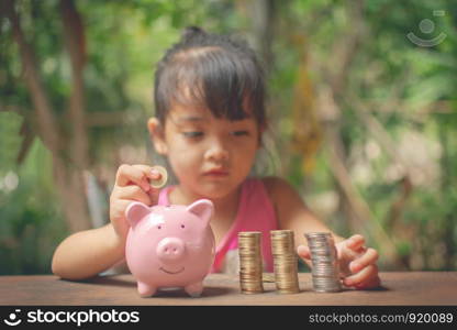 cute little girl holding coin of money and put in pink piggy bank with blur background. subject is blurred.