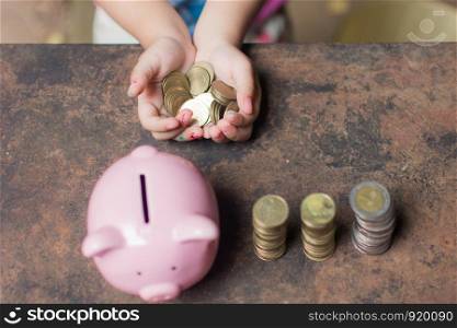 cute little girl holding coin of money and put in pink piggy bank with blur background. subject is blurred.