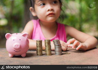 cute little girl holding coin of money and put in pink piggy bank with blur background. subject is blurred.