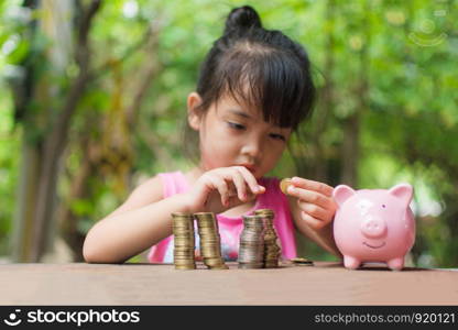 cute little girl holding coin of money and put in pink piggy bank with blur background. subject is blurred.