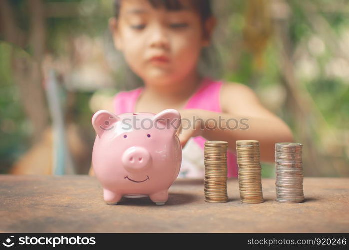 cute little girl holding coin of money and put in pink piggy bank with blur background. subject is blurred.