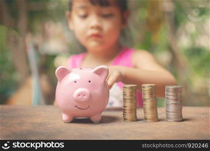 cute little girl holding coin of money and put in pink piggy bank with blur background. subject is blurred.