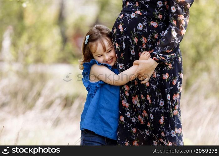 Cute little girl hugging and kissing her mother&rsquo;s pregnant belly in spring nature.. Cute little girl hugging and kissing her mother&rsquo;s pregnant belly in spring nature
