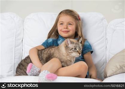 Cute little girl hugging tabby cat with love, looking away.