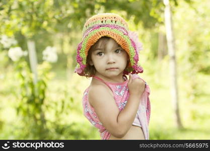 Cute little girl in a summer grove with a bright cap on her head