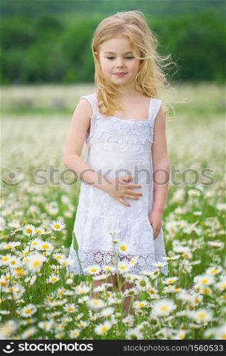 Cute little girl in big camomile meadow. Portrait composition.