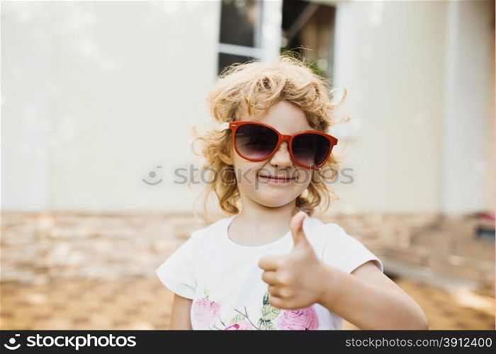 Cute little girl in red sunglasses showing a thumbs up