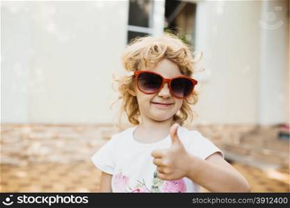 Cute little girl in red sunglasses showing a thumbs up