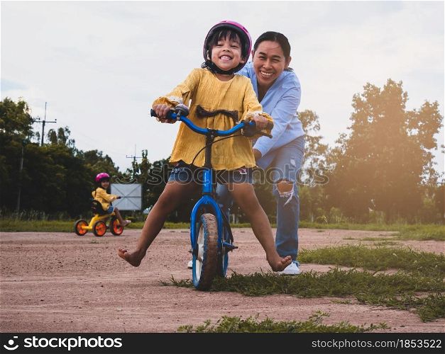 Cute little girl in safety helmet learn to ride a bike with her mother in summer park. Outdoor sports for kids. childhood happiness. family spending time together.