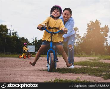 Cute little girl in safety helmet learn to ride a bike with her mother in summer park. Outdoor sports for kids. childhood happiness. family spending time together.