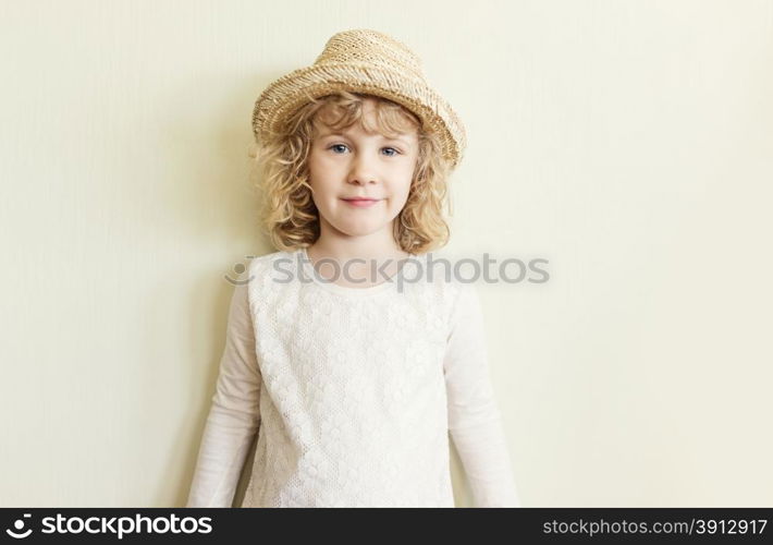 Cute little girl in straw hat standing near wall