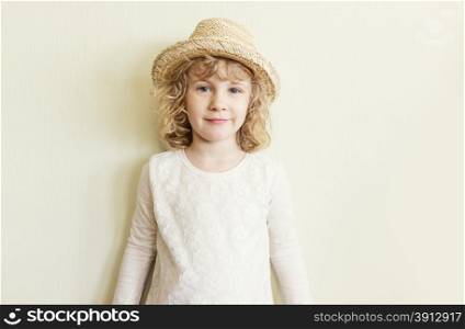 Cute little girl in straw hat standing near wall