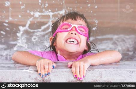 Cute little girl in swim glasses having fun in swimming pool. Children enjoy outdoor activities on hot summer days.