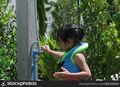 Cute little girl in swimming suits frolicking in the outdoor shower. Happy little girl enjoying in summer day and playing with water.