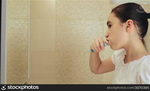 Cute little girl intensely brushing her teeth in the bathroom.