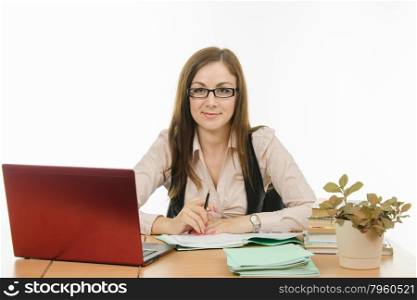 Cute little girl is a teacher sitting at a desk with a laptop, books and notebooks