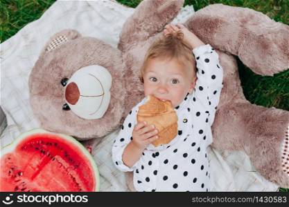 cute little girl is eat croissant lying on blanket on picnic. happy summer holiday. Concept of childhood and tenderness.. cute little girl is eat croissant lying on blanket on picnic. happy summer holiday. Concept of childhood and tenderness