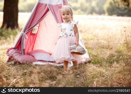 cute little girl is having fun near wigwam in a summer field on sunny day. Young family spending time together on vacation, outdoors. The concept of summer holiday.. cute little girl is having fun near wigwam in a summer field on sunny day. Young family spending time together on vacation, outdoors. The concept of summer holiday