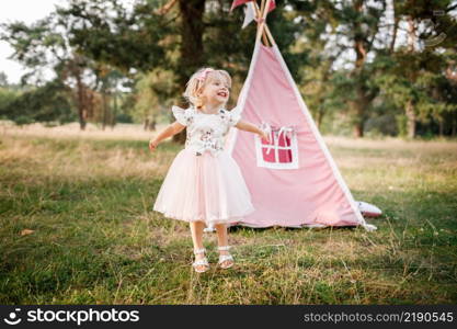 cute little girl is having fun near wigwam in a summer field on sunny day. Young family spending time together on vacation, outdoors. The concept of summer holiday.. cute little girl is having fun near wigwam in a summer field on sunny day. Young family spending time together on vacation, outdoors. The concept of summer holiday