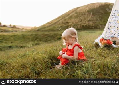 cute little girl is having fun near wigwam in a summer field on sunset. Young family spending time together on vacation, outdoors. The concept of summer holiday. cute little girl is having fun near wigwam in a summer field on sunset. Young family spending time together on vacation, outdoors. The concept of summer holiday.