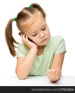 Cute little girl is talking on a cell phone while sitting at table, isolated over white