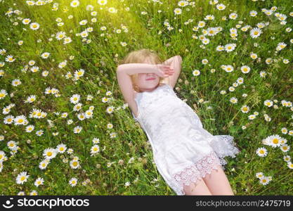 Cute little girl lie in big camomile meadow. Portrait composition.