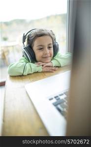 Cute little girl listening to music on headphones while using laptop at home