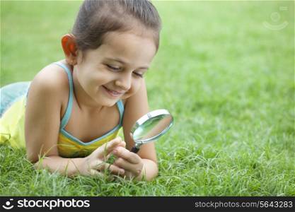 Cute little girl looking through magnifying glass in the park