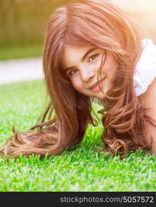 Cute little girl lying down on fresh green grass field, having fun outdoors, relaxing on backyard, happy and carefree childhood