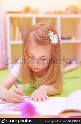 Cute little girl lying down on the floor and drawing picture to the album, having fun at home, happy childhood, having art talent concept