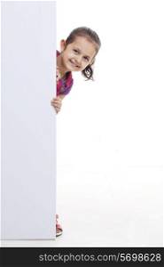Cute little girl peeking through blank billboard