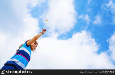 Cute little girl playing with wind kite outdoors, sweet child on blue sky background, having fun in summer day, happy childhood concept