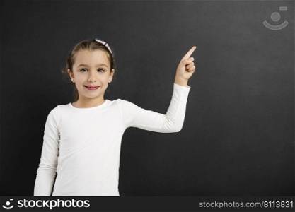 Cute little girl pointing to a blackboard, with copy space.