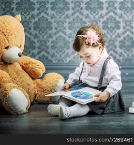 Cute little girl reading a book sitting on the dark floor
