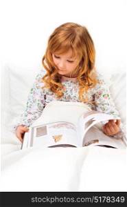 Cute little girl reading before sleep in her bed with white linen