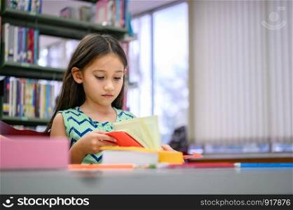Cute little girl reading books in library attentively at school. Girl concentrating to learning by herself outside classroom. Education and People lifestyles. Academic and Kids duty concept.