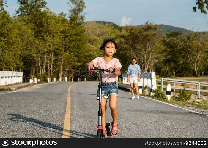 Cute little girl riding scooter on road in outdoor park. Healthy sports and outdoor activities for school children in the summer.