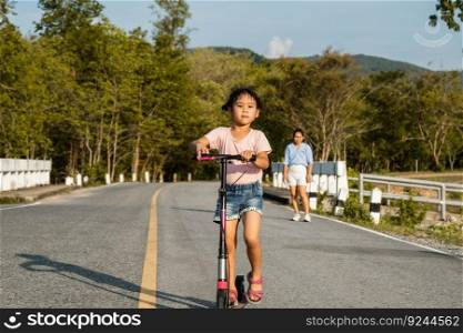 Cute little girl riding scooter on road in outdoor park. Healthy sports and outdoor activities for school children in the summer.