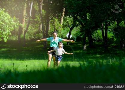 Cute little girl runs with her mother spreading her arms as if flying in a spring garden. Young mother playing with her daughter in the park. Happy family having fun in the park.