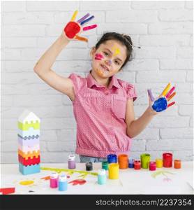 cute little girl showing painted hands standing front table with colorful colors
