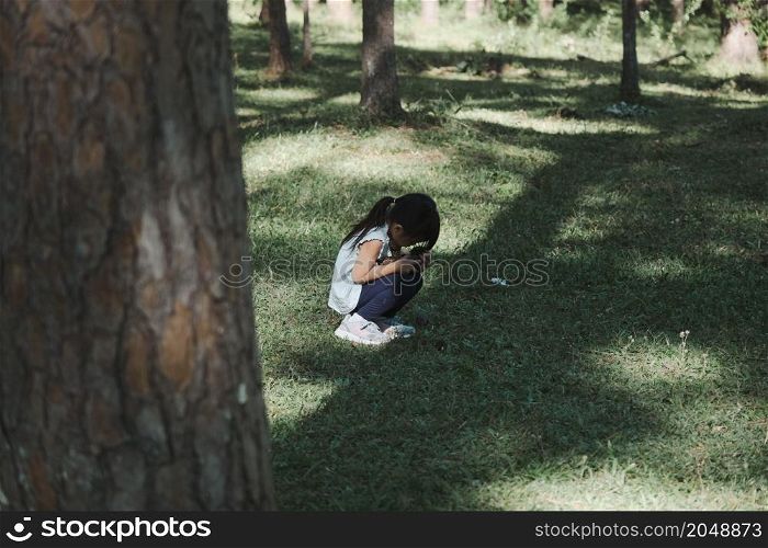 Cute little girl sits on the grass with her eyes closed while playing hide and seek with her family in the park. Happy child spending time with her family on vacation.