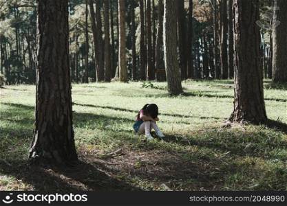Cute little girl sits on the grass with her eyes closed while playing hide and seek with her family in the park. Happy child spending time with her family on vacation.