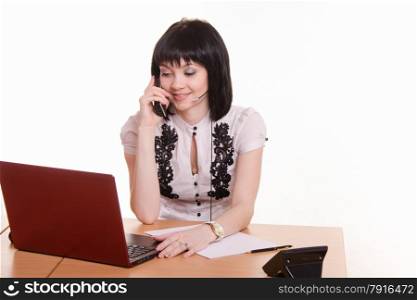 Cute little girl sitting at a table in a call center with a laptop in a white blouse with a phone in his hand. Office employee call-center friendly talking on the phone